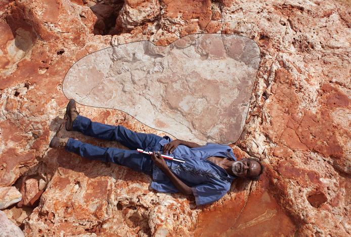 Ležící Richard Hunter z kmene Goolarabooloo spolu s největším otiskem chodidla býložravého sauropoda. Tyčka, kterou drží, je dlouhá 40 cm (foto University of Queensland).